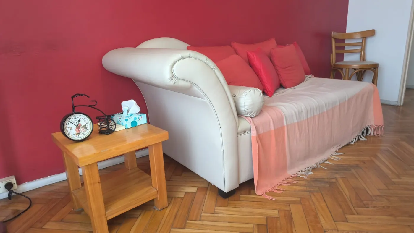 Diván blanco con almohadones rojos y mesa de luz